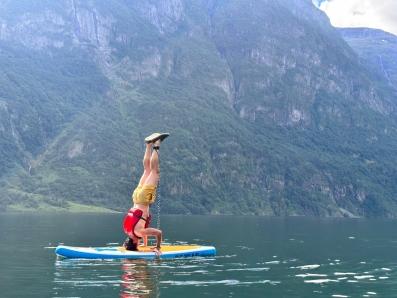 Sur un lac avec les montagnes en arrière plan, un homme fait le poirier sur une planche